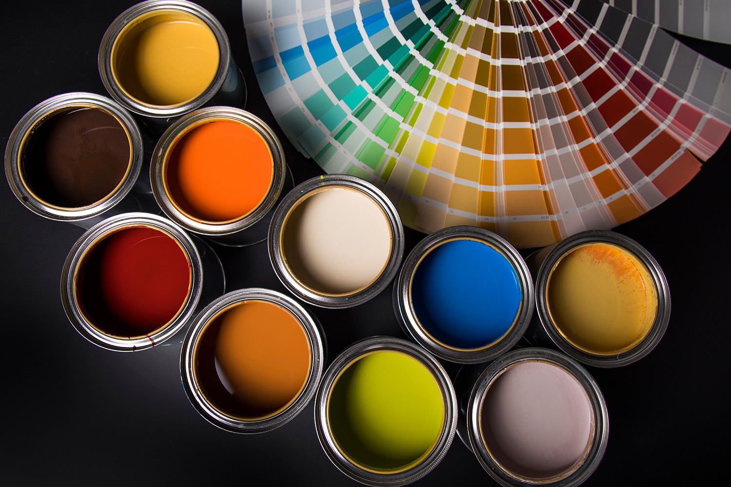 Paint cans in two rows showing multiple colors of paint filled in each can. Behind the cans, color swatches laid out in a fan, various colors.